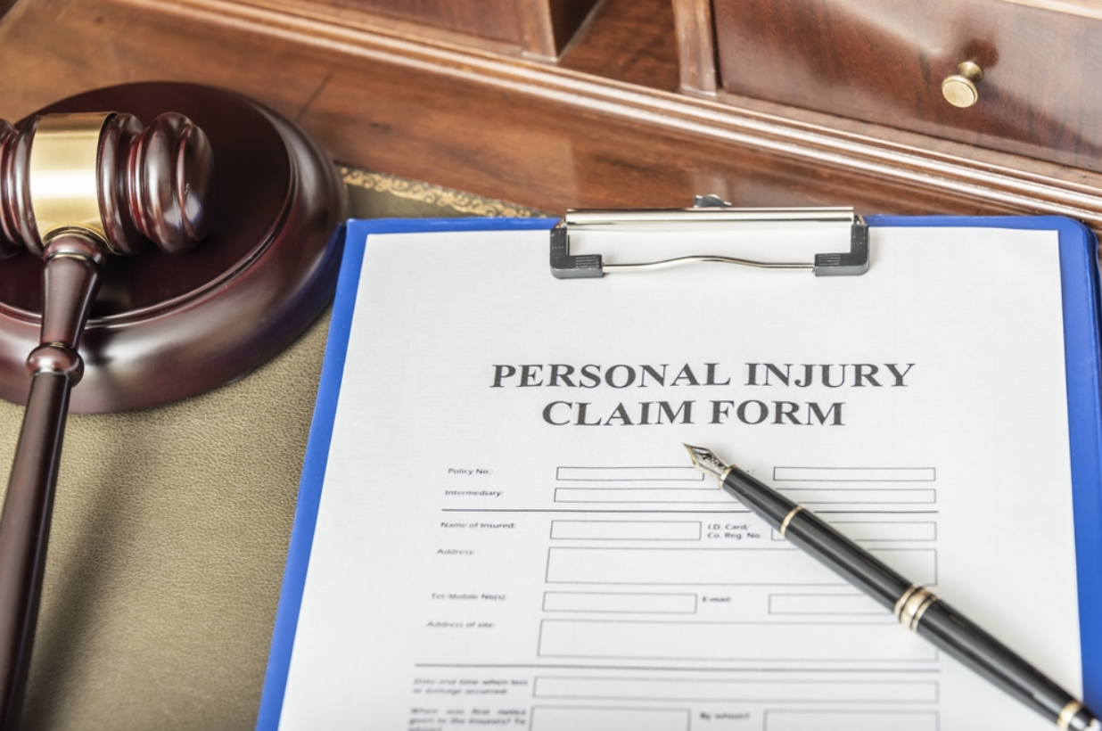 A personal injury claim form on a clipboard with a pen placed on top, next to a judge’s gavel, symbolizing legal action and personal injury lawsuits.