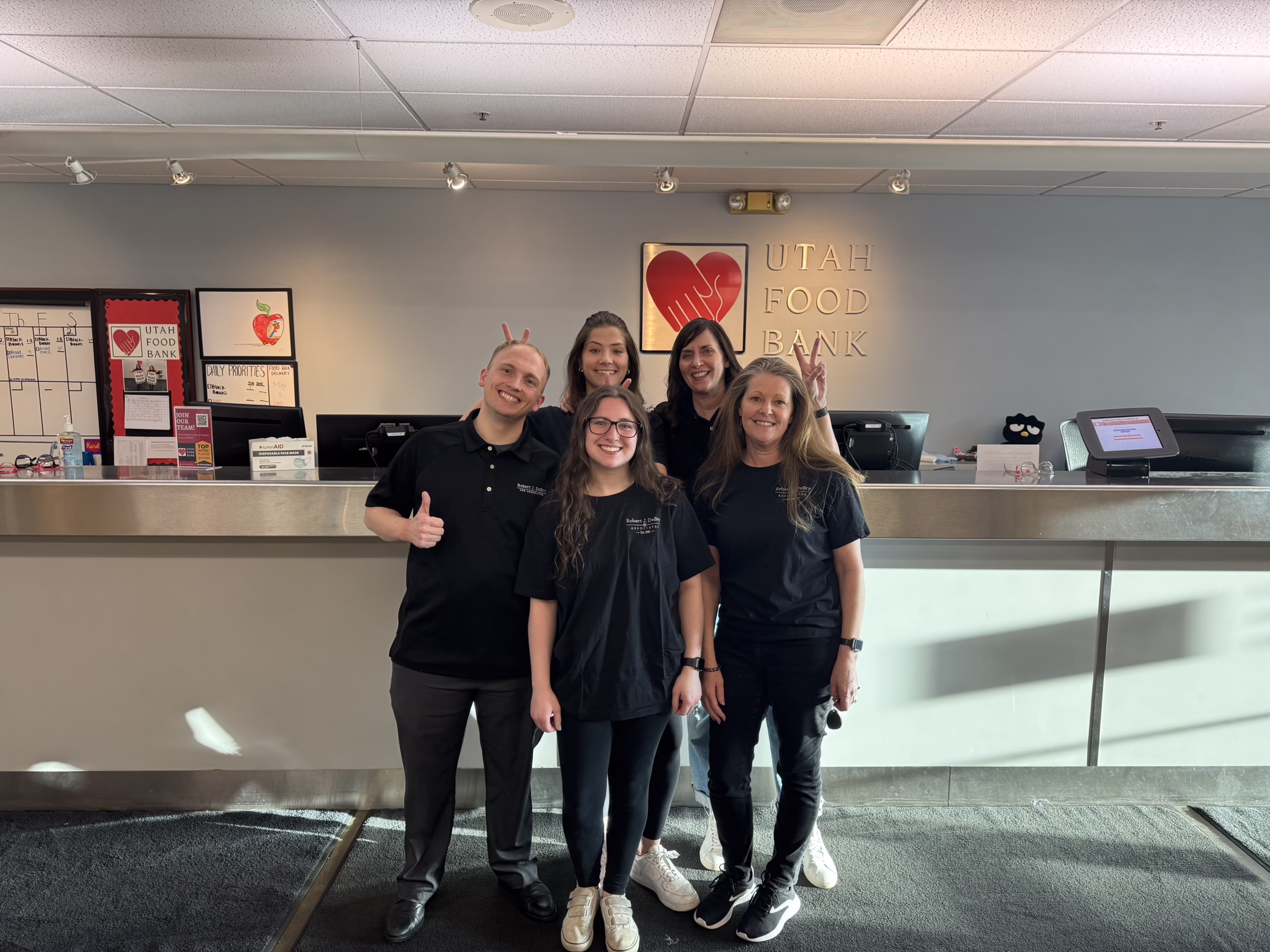 Five Robert J. DeBry and Associates staff members in firm shirts at the Utah Food Bank front desk